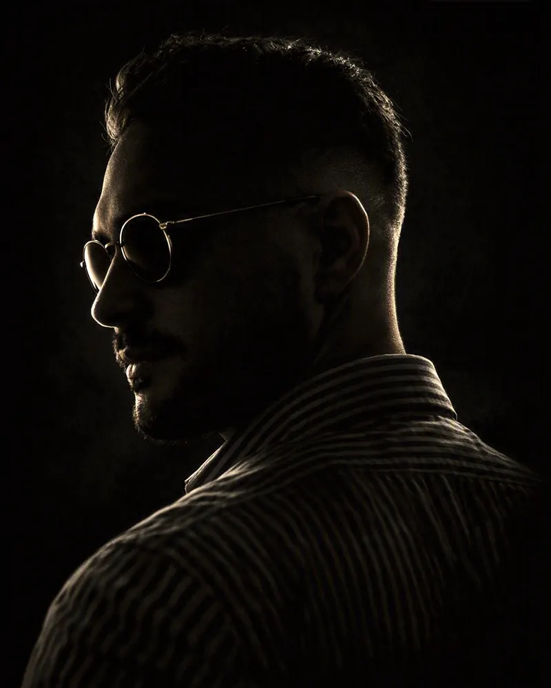 Portrait d'Eliot Ferret, de profil, en contre-jour, avec des lunettes rondes